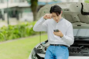 A man on the phone while standing in front of his broken vehicle.